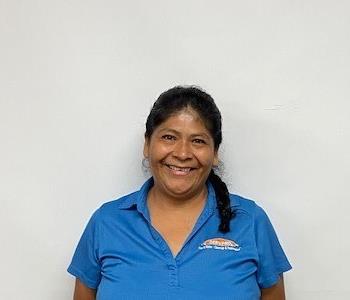 Black haired hispanic female in a light blue polo standing in front of a white background